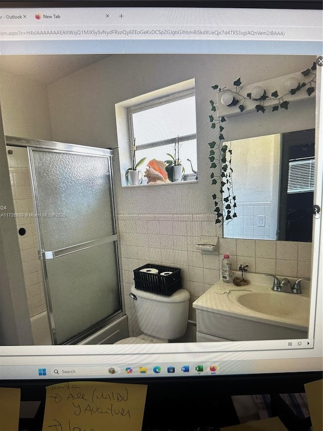 full bathroom featuring shower / bath combination with glass door, tile walls, toilet, backsplash, and vanity