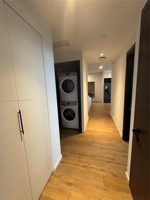 corridor with stacked washing maching and dryer and light hardwood / wood-style flooring