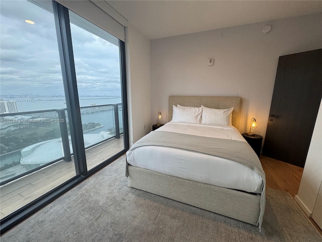 bedroom with wood-type flooring, access to exterior, and a water view