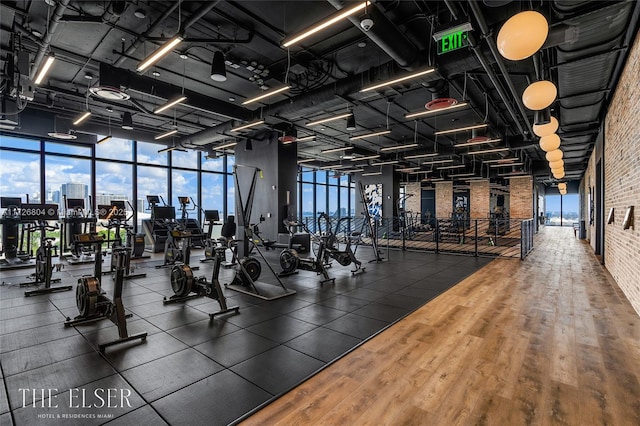 exercise room featuring brick wall, a wall of windows, and dark wood-type flooring