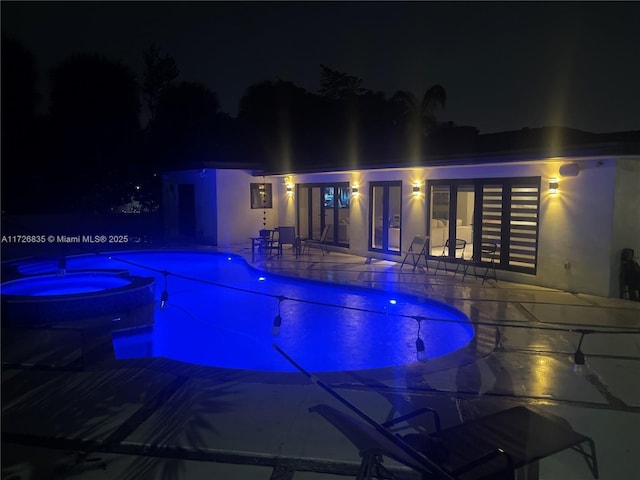 pool at night featuring a patio and an in ground hot tub