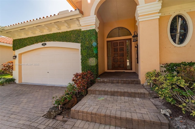 view of exterior entry with a garage, driveway, and stucco siding