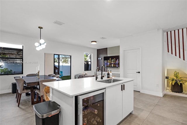 kitchen featuring a center island with sink, beverage cooler, pendant lighting, white cabinets, and sink