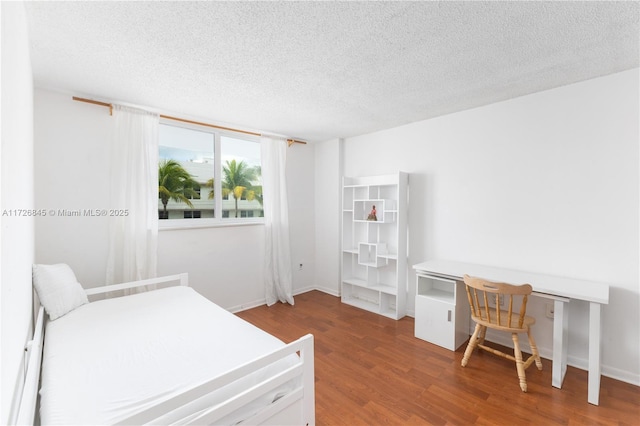 bedroom featuring baseboards, a textured ceiling, and wood finished floors