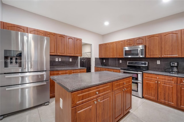 kitchen with light tile patterned floors, appliances with stainless steel finishes, a center island, tasteful backsplash, and separate washer and dryer