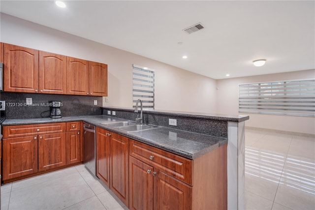 kitchen with sink, dark stone countertops, light tile patterned floors, stainless steel dishwasher, and kitchen peninsula