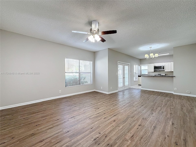 unfurnished living room with a wealth of natural light, ceiling fan with notable chandelier, a textured ceiling, and light wood-type flooring