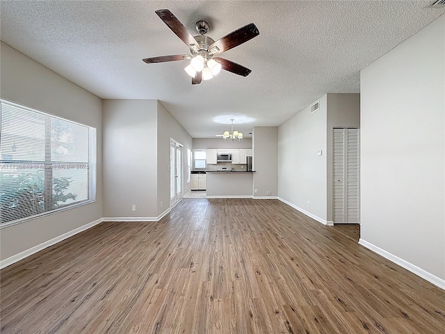 unfurnished living room featuring hardwood / wood-style flooring, ceiling fan with notable chandelier, and a textured ceiling