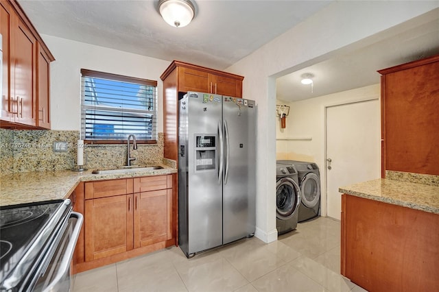 kitchen featuring washing machine and clothes dryer, appliances with stainless steel finishes, tasteful backsplash, light stone countertops, and sink