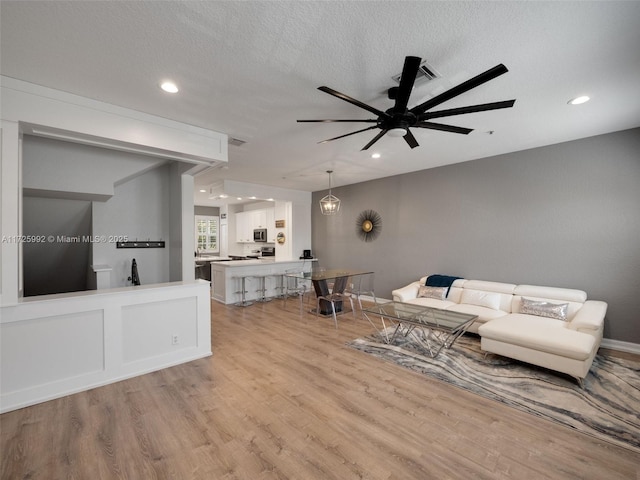 living room with a textured ceiling, ceiling fan, and light hardwood / wood-style flooring