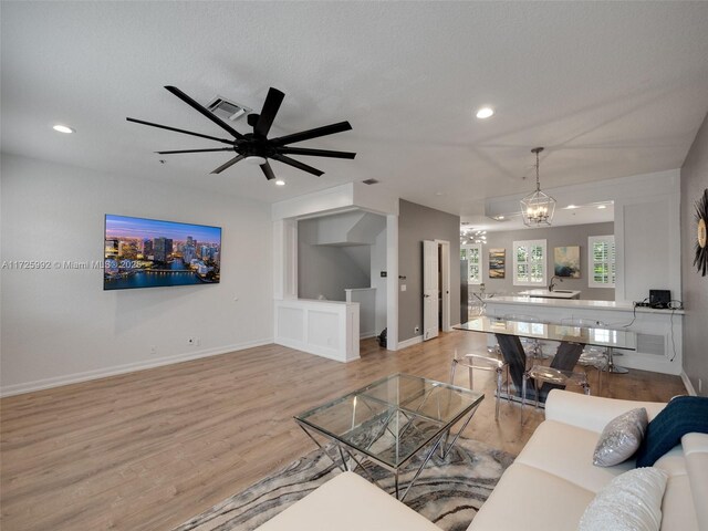 living room featuring a textured ceiling, light wood-type flooring, built in features, and ceiling fan with notable chandelier