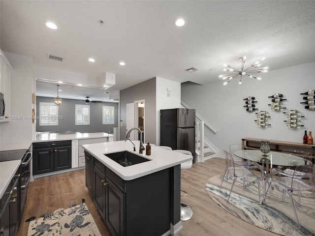 kitchen featuring a kitchen island with sink, refrigerator, sink, light hardwood / wood-style flooring, and ceiling fan with notable chandelier