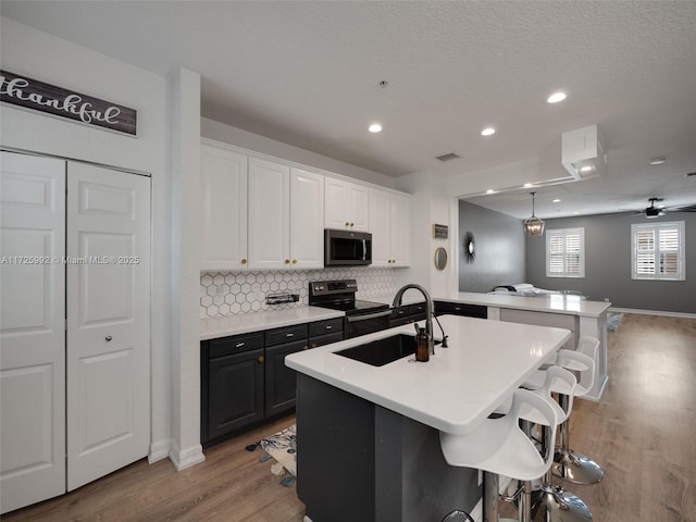 kitchen featuring a center island with sink, white cabinets, appliances with stainless steel finishes, a kitchen breakfast bar, and sink