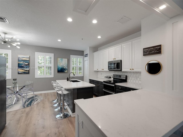 kitchen with a center island with sink, white cabinetry, appliances with stainless steel finishes, a kitchen breakfast bar, and sink