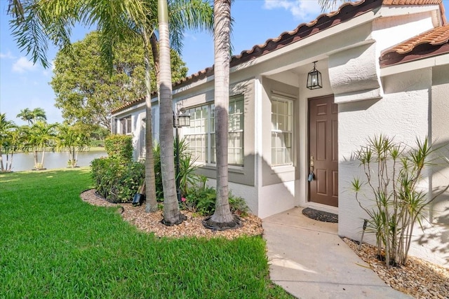 doorway to property with a yard, stucco siding, a water view, and a tiled roof