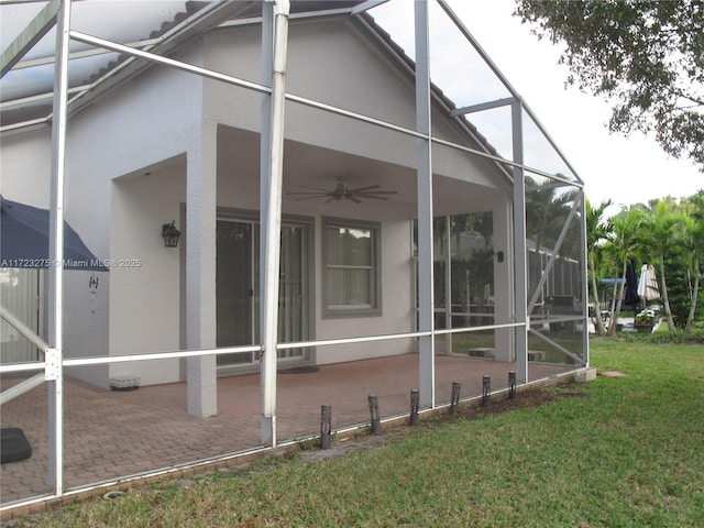 view of side of property with glass enclosure, a patio area, a lawn, and ceiling fan