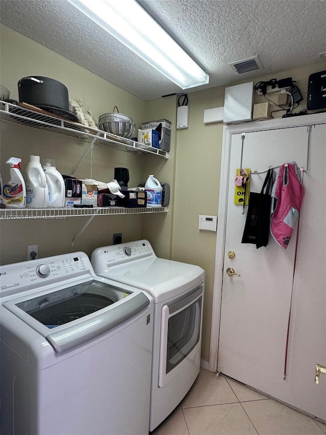 laundry area featuring a textured ceiling, light tile patterned floors, and washer and clothes dryer