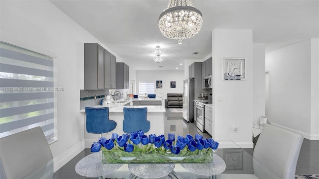 kitchen with gray cabinets, kitchen peninsula, sink, appliances with stainless steel finishes, and a chandelier