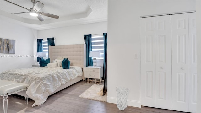 bedroom with ceiling fan, a tray ceiling, a closet, wood-type flooring, and a textured ceiling