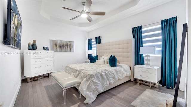 bedroom with a raised ceiling, ceiling fan, multiple windows, and wood-type flooring