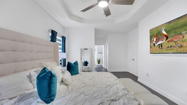 bedroom with a raised ceiling, ceiling fan, and dark hardwood / wood-style floors