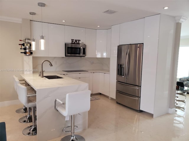 kitchen featuring appliances with stainless steel finishes, white cabinets, sink, hanging light fixtures, and a breakfast bar