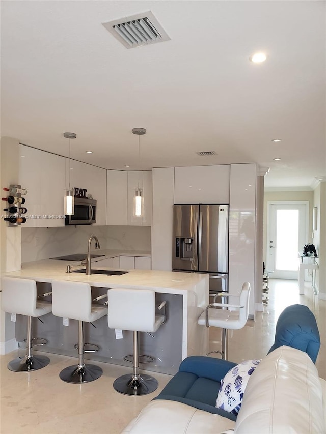 kitchen with sink, hanging light fixtures, appliances with stainless steel finishes, a breakfast bar area, and white cabinets