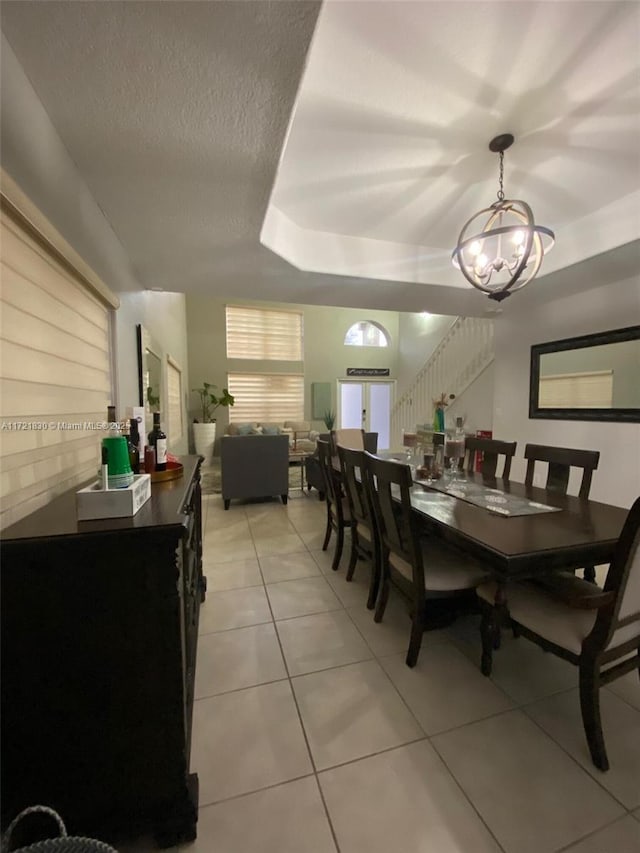 dining space with light tile patterned flooring, a raised ceiling, an inviting chandelier, and a textured ceiling