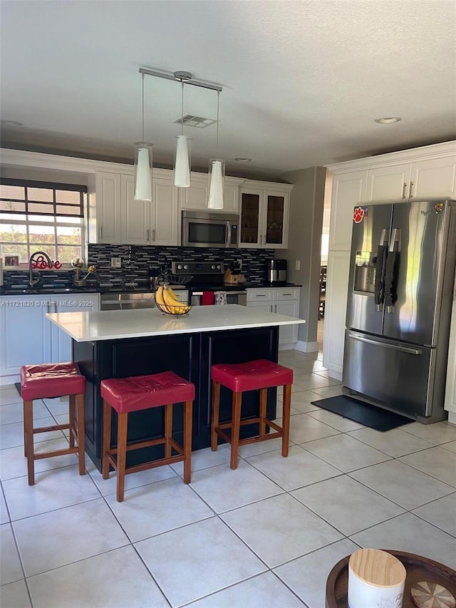 kitchen with appliances with stainless steel finishes, backsplash, a kitchen bar, hanging light fixtures, and a center island