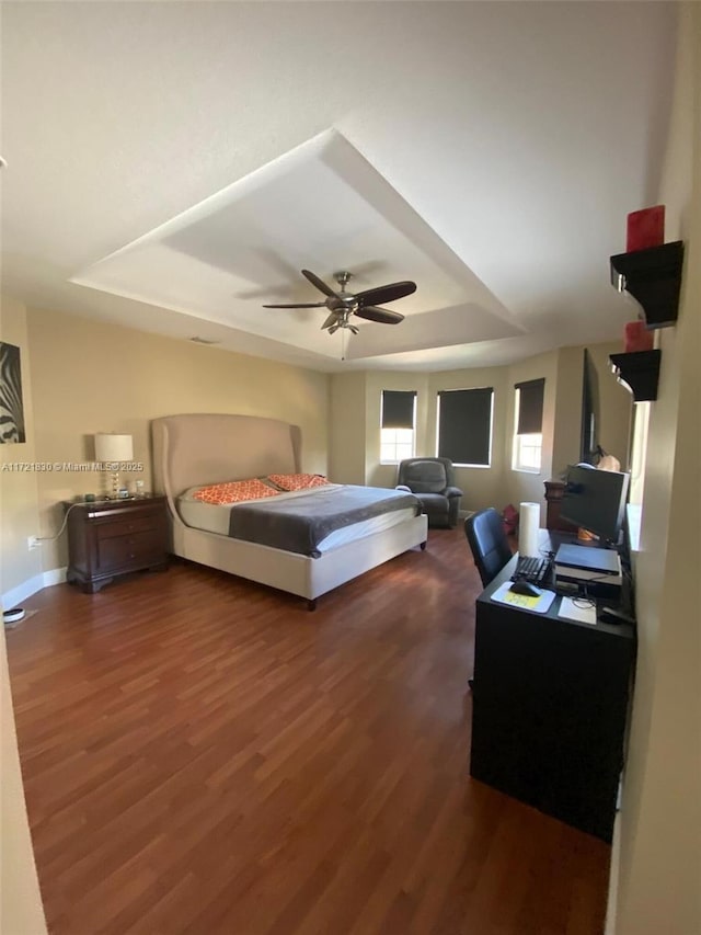 bedroom with a tray ceiling, dark hardwood / wood-style floors, and ceiling fan