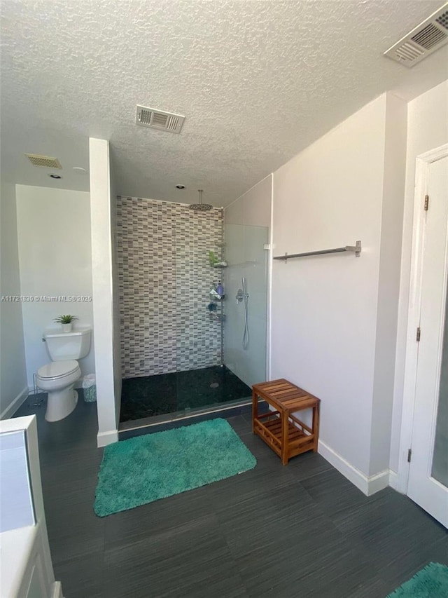 bathroom featuring tiled shower, wood-type flooring, toilet, and a textured ceiling