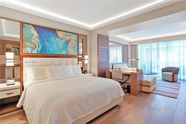 bedroom with light hardwood / wood-style floors and a tray ceiling