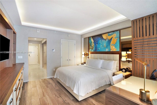 bedroom with a closet, light hardwood / wood-style floors, and a raised ceiling