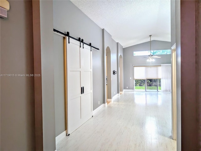 hallway featuring a barn door, lofted ceiling, a textured ceiling, and light hardwood / wood-style flooring