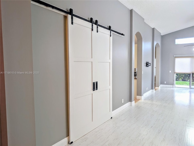 hallway featuring a barn door, lofted ceiling, a textured ceiling, and light wood-type flooring