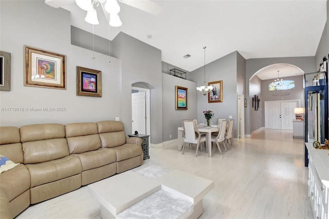 living room with ceiling fan with notable chandelier, a high ceiling, and light wood-type flooring