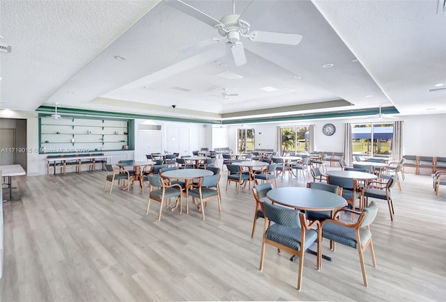 dining area featuring a raised ceiling, a textured ceiling, and light hardwood / wood-style floors