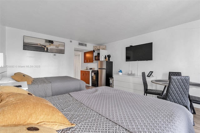 bedroom with stainless steel refrigerator and light hardwood / wood-style flooring