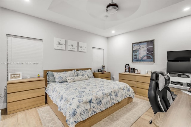 bedroom featuring ceiling fan, a tray ceiling, and light wood-type flooring