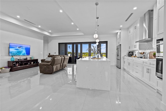 kitchen featuring white cabinetry, an island with sink, hanging light fixtures, and wall chimney range hood