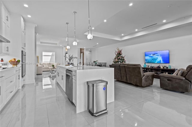 kitchen featuring a raised ceiling, white cabinets, and a center island with sink