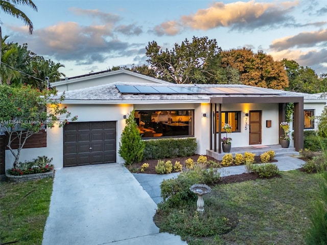 view of front facade featuring a garage, a lawn, solar panels, and covered porch