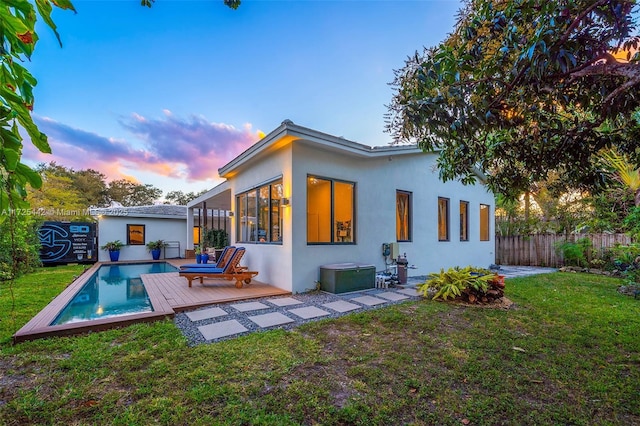 back house at dusk with a fenced in pool and a yard