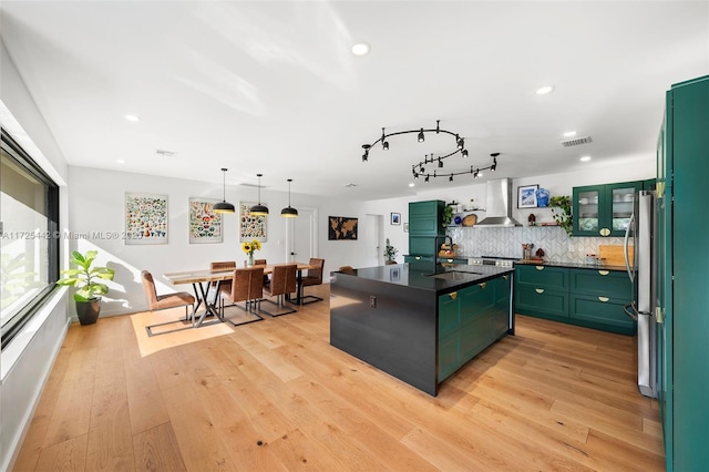 kitchen featuring wall chimney exhaust hood, green cabinets, and light hardwood / wood-style flooring