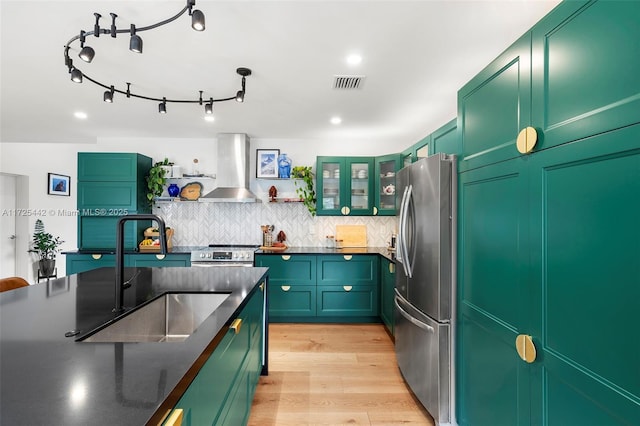 kitchen featuring appliances with stainless steel finishes, wall chimney range hood, decorative backsplash, sink, and light wood-type flooring