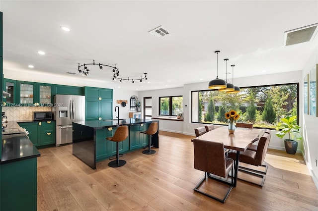 kitchen featuring stainless steel refrigerator with ice dispenser, decorative light fixtures, sink, a kitchen breakfast bar, and light wood-type flooring