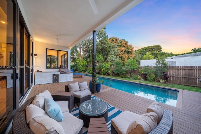 pool at dusk featuring a wooden deck, outdoor lounge area, and ceiling fan