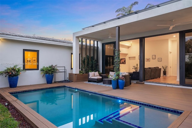 pool at dusk featuring ceiling fan, a wooden deck, and outdoor lounge area