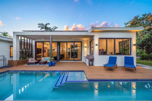 back house at dusk featuring ceiling fan, an outdoor living space, and a pool side deck