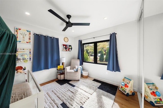 bedroom with ceiling fan, wood-type flooring, and a crib